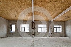 Unfinished apartment or house big loft room under reconstruction. Plywood ceiling, plastered walls, window openings, cement floor