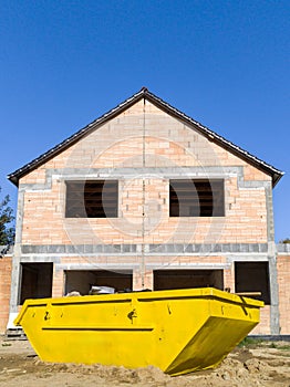 Unfinished brick house with construction skip in front
