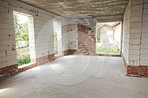 Unfinished house inside. Aerated concrete blocks wall with windows, doorways and concrete floor in sunny day. Process of house