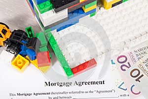 Unfinished house made of toy blocks, miniature excavator, polish currency money, mortgage agreement form. Renting real estate and