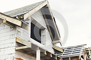 Unfinished house. Wooden roof framing with vapor barrier and dormer on block walls with windows. New modern farmhouse construction