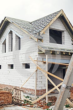 Unfinished house. Wooden roof framing with vapor barrier and dormer on block walls with windows. New modern farmhouse construction