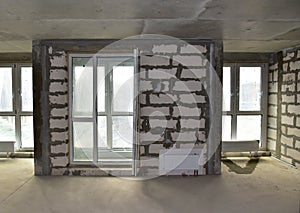 Unfinished interior of apartment under construction with gray concrete wall and double-glazed windows in a residential multi-