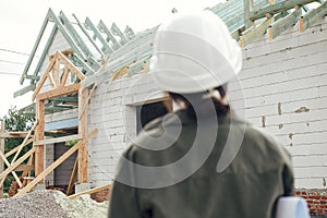 Unfinished modern farmhouse and blurred image of stylish woman architect with blueprints at construction site. Young female