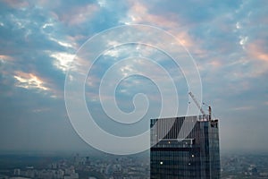 Unfinished skyscraper construction and tower crane against dramatic evening sky