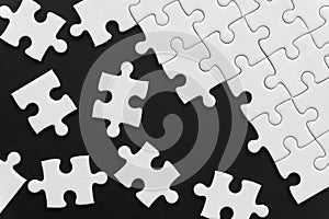 Unfinished white jigsaw puzzle pieces on black background