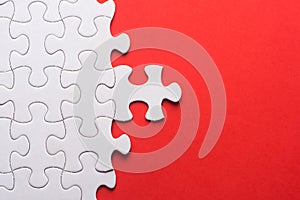 Unfinished white jigsaw puzzle pieces on red background