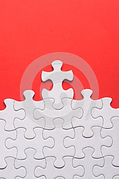 Unfinished white jigsaw puzzle pieces on red background