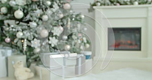 Unfocused classic white room with Christmas and New Year interior decoration and fireplace. Green tree decorated with