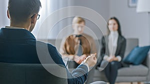 Unfocused Couple on Counseling Session with Psychotherapist. Focus on Back of Therapist Taking Notes