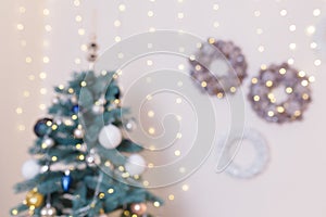 Unfocused shot. Blurry Christmas background with decorated fir-tree and  hanging pine cone wreaths with golden garland lights