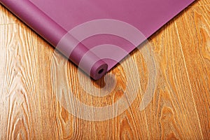 An unfolded lilac-colored yoga mat is unfolded on the wooden floor