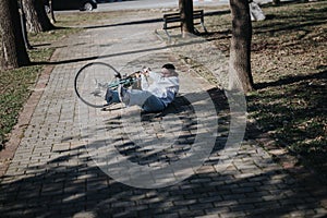 Unfortunate cyclist lying on ground after a bicycle accident in the park.