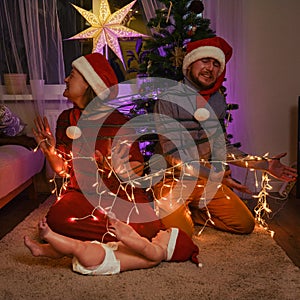 Unfree parents with a small child on New Year Eve. A family with a newborn baby at the Christmas tree in the evening living room