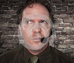 Unfriendly Businessman with Frowning Face Wearing Phone Headset In Office with Brick Background