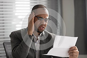 Unhappy African American businessman reading document, receiving bad news