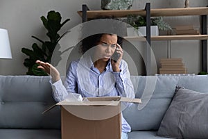Unhappy African American woman talking on phone, complaining on shipment