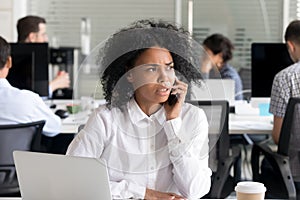 Unhappy African American woman talking on phone at workplace