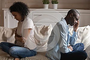 Unhappy african couple ignoring each other sitting separately on couch