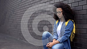 Unhappy african school girl sitting campus, puberty age loneliness, insecurities