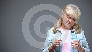 Unhappy aged lady holding pills unwilling to take them, ineffective medication