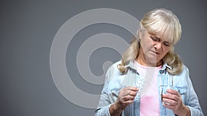 Unhappy aged lady holding pills unwilling to take them, ineffective medication photo