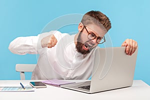 Unhappy aggressive man office worker screaming holding fist clenched, going to hit laptop display, bugs and errors in operating