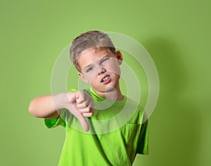 Unhappy, angry, displeased child giving thumbs down hand gesture, isolated on green background.