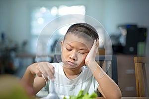 Unhappy Asian Boy eating vegetables at table.