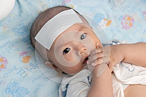 Unhappy Asian Chinese little baby child sick suffering heat from fever with cool fever jel pad on forehead