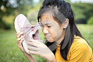 Unhappy asian female teenage is sniffing her sneakers,hold stinky shoe in her hand with disgust,unpleasant smell because of hot