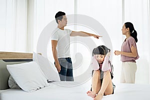 Unhappy asian girl child cover her ears with parents having argument in the background