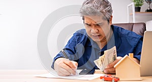 Unhappy Asian man holding a banknote and Making an account of income and expenses to pay the home loan and car loan, Concept loan