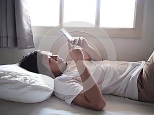 Unhappy Asian man with mobile smart phone lying down on the bed.