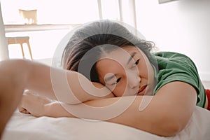 Unhappy asian Thai woman leaning on white cough sofa while resting head on arm with sadness sitting on wooden floor