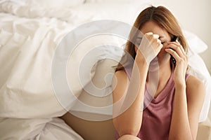 Unhappy asian woman sitting on bedroom floor, covering face with hand and using smartphone with worried expression at bedroom