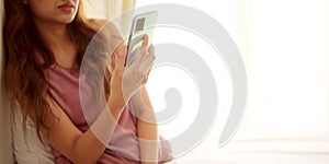 Unhappy asian woman using smartphone and sitting on bedroom floor with worried expression at bedroom