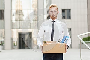 Unhappy bearded business man going out with cardboard, looking at camera and feeling looser.