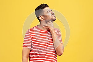 Unhappy bearded man in striped t-shirt grimacing touching his neck, feeling pain while swallowing, sore throat, risk of choking or