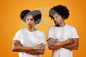Unhappy black man looking at his upset wife, orange background