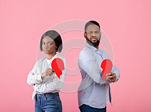 Unhappy black man and woman holding halves of broken heart on pink studio background