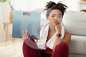Unhappy Black Woman Holding Weight-Scales After Slimming Failure At Home