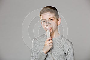 Unhappy boy breathing through inhalator mask photo