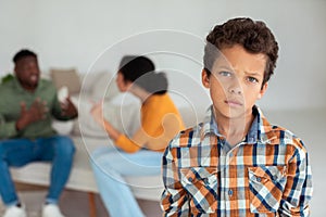 Unhappy boy looking at camera while parents fighting on background