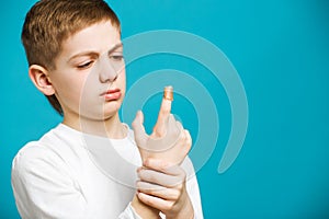 Unhappy boy in white clothes with adhesive plaster on his finger