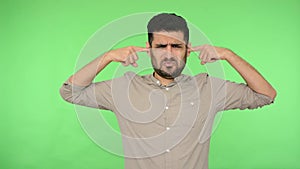 Unhappy brunette man with bristle in shirt shutting ears by forefinger, saying no, don`t want to hear, looking at camera with disp