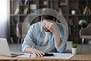 Unhappy businessman in glasses calculating bills, worried by financial problem