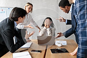 Unhappy Businesswoman Covering Face While Coworkers Shouting At Her Indoors