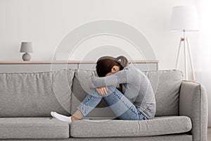 Unhappy caucasian millennial woman suffering from depression and loneliness, sitting on sofa at home