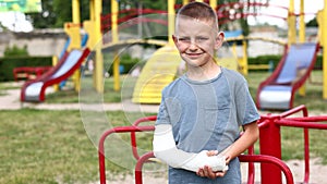unhappy child with broken limb arm outdoors on playground background. school boy had accident on summer vacation. kid in
